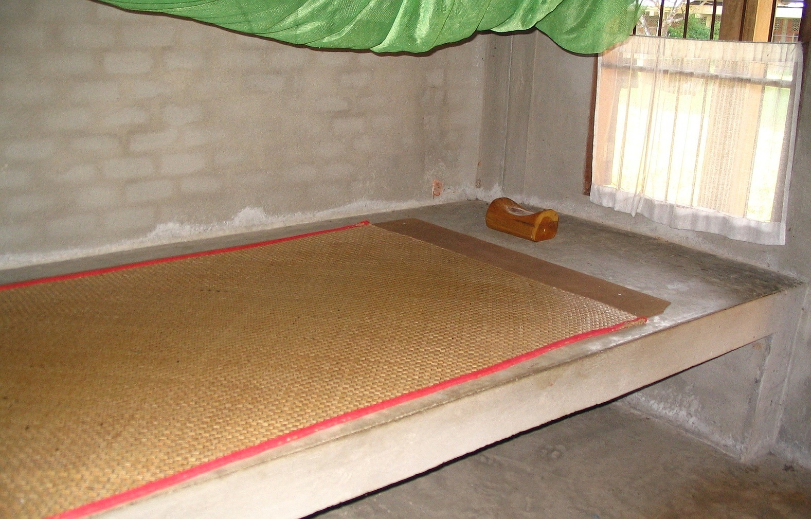 Betonová postel, rohož, moskytiéra a dřevěný polštářek - Wat Suan Mokkh - Thajsko