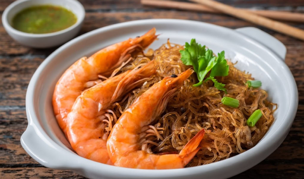 Smažené krevety s skleněnými nudlemi a čerstvou petrželí na talíři. Autentická thajská a kambodžská kuchyně s chutí moře.